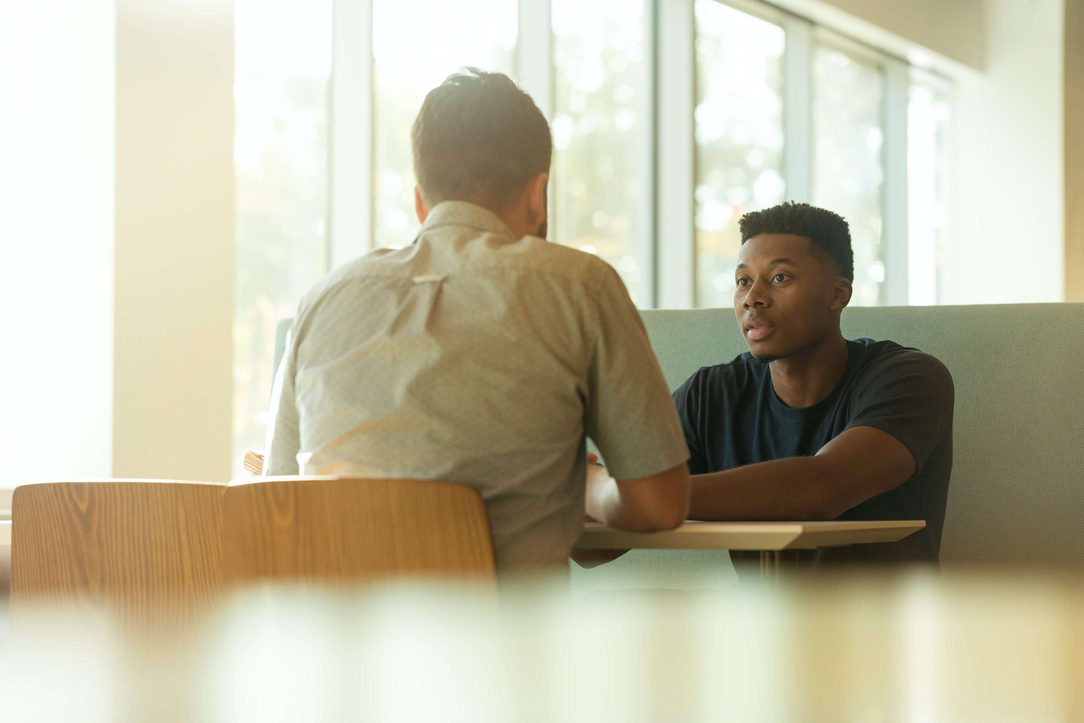 Two young men have a conversation while sitting at a table.