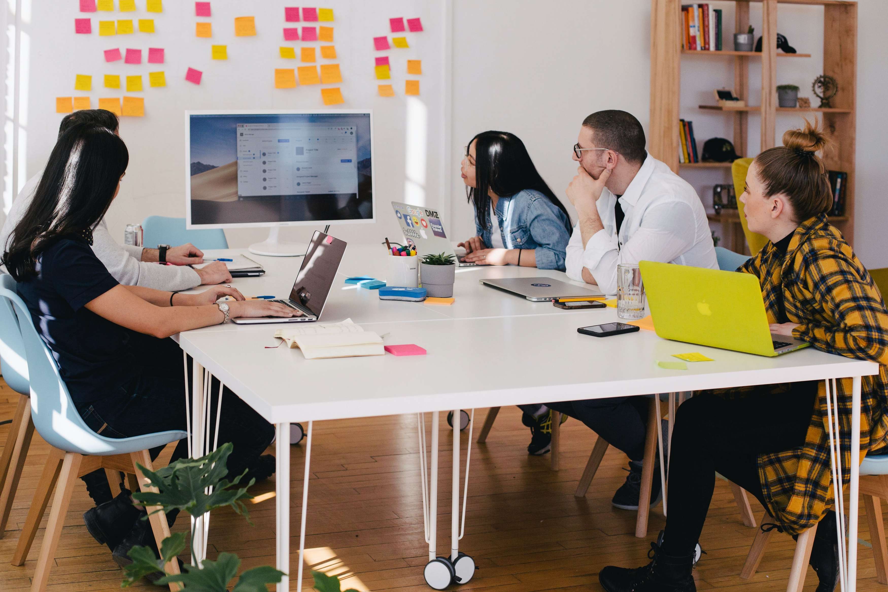 A group of young adults sit around a table looking at a computer screen in a collaborative work space.