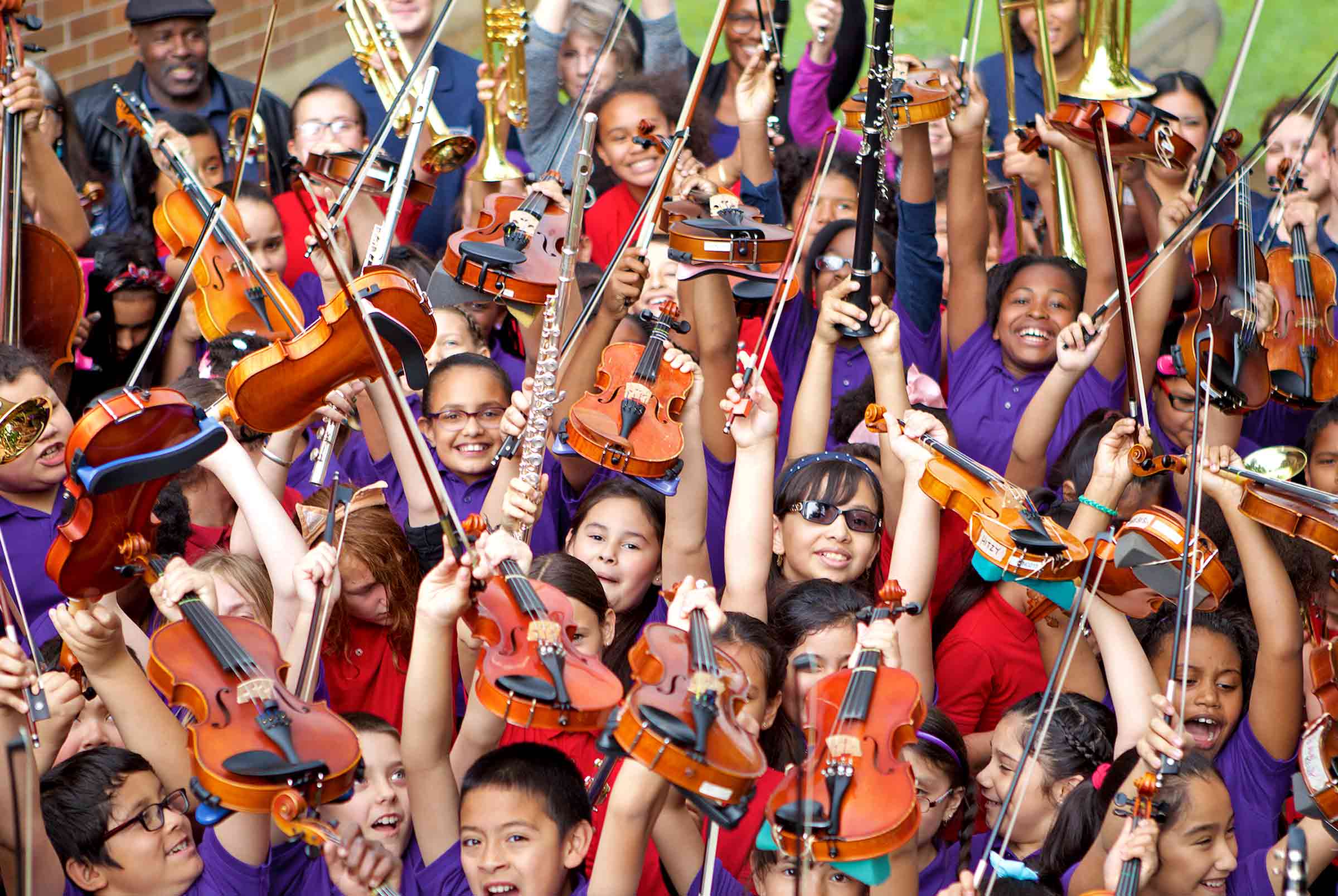 A group of children wearing purple shirts hold up instruments and smile for the camera.