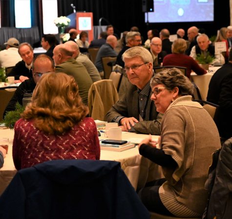 A man and a woman listen to another woman talking at a table at the Leadership Now 2022 conference.