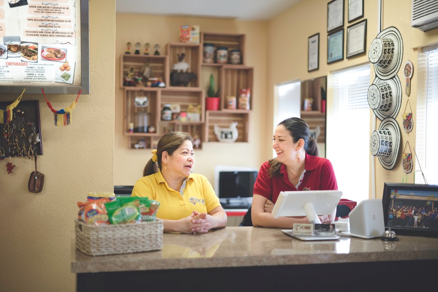 Two women have a conversation at a restaurant register.