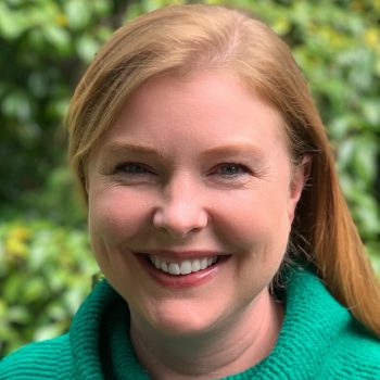 A woman in a green turtleneck sweater smiles for the camera.