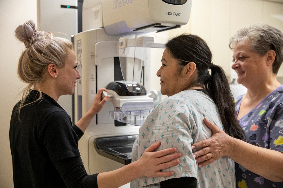 Two nurses place their hands on the back of a patient about to get a mammogram