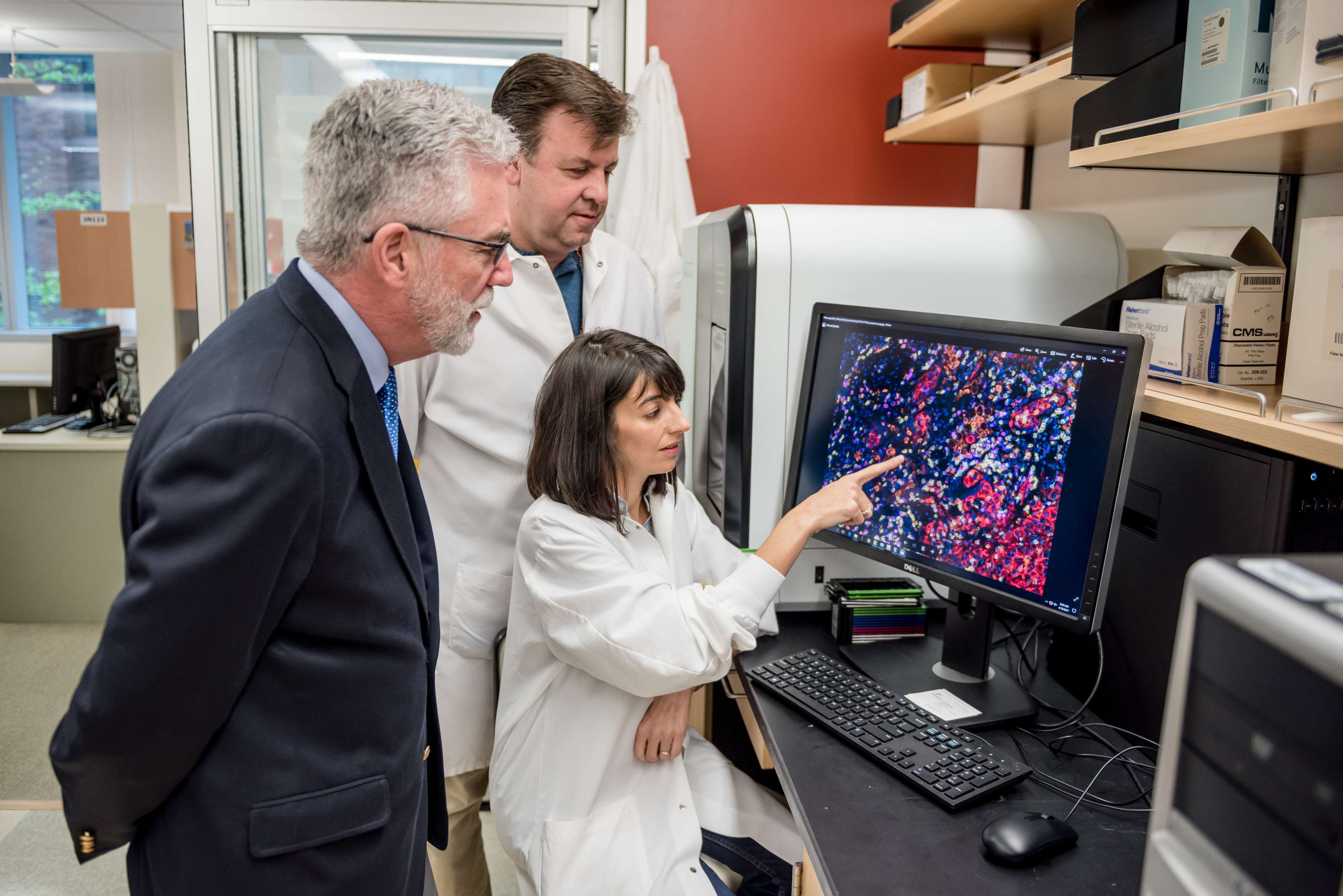 Three people look at a computer showing cells, with one pointing at the screen.