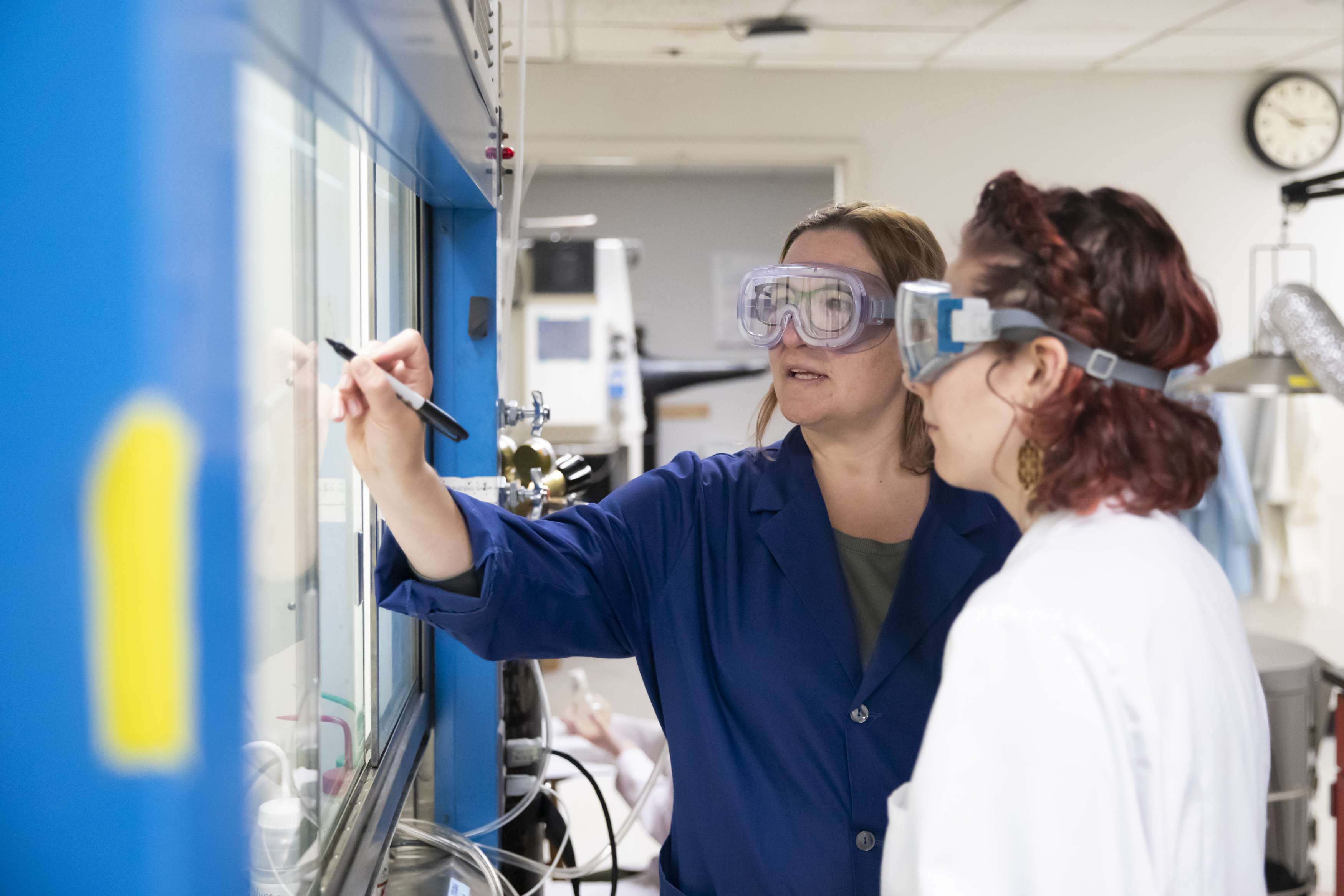 Two women wearing protective eyewear with one woman writing with a sharpie