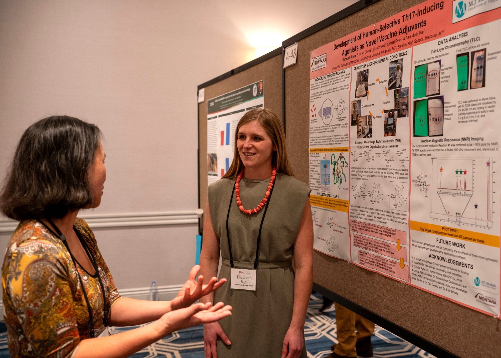 Two individuals engaging in a discussion at a scientific conference poster session. One person is standing by a poster that includes various graphs and diagrams related to vaccine development.