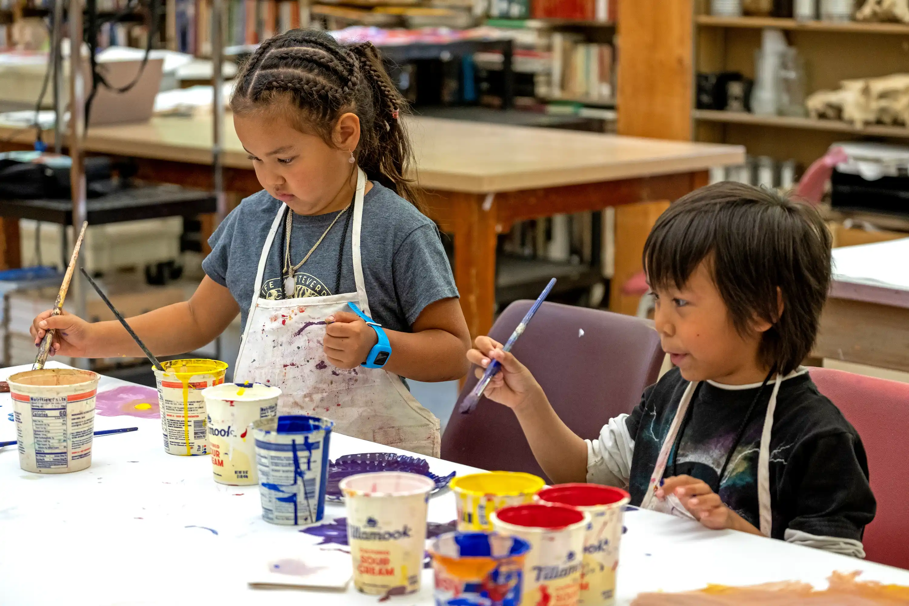 two children seated at a table painting