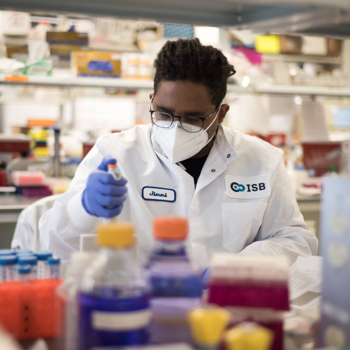 Biologist working in lab wearing a mask, gloves, and white lab coat
