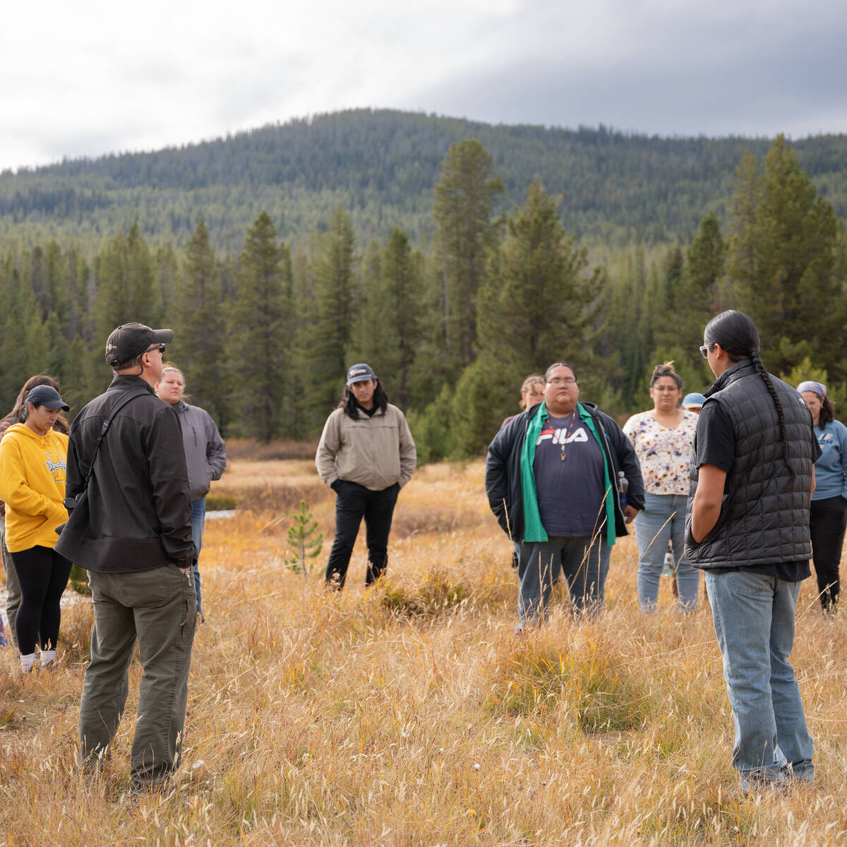 Group of people in a dry grassy field with trees in the background