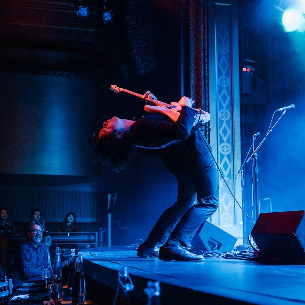 Person playing guitar on a stage with smoke and blue lights, engaged in an energetic performance.