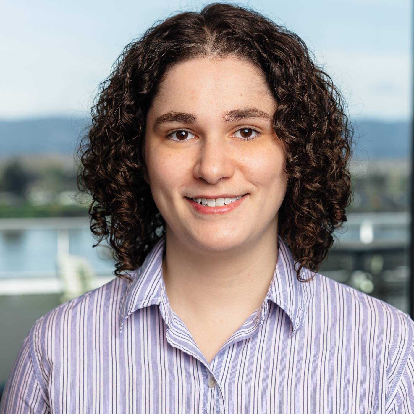 Smiling headshot of person in a collared shirt, with a light background behind them.