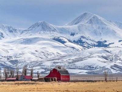 Montana farm landscape with a red barn in the foreground and snowy mountains in the background