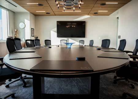 A board room with a large round table, 10 seats around the table, and a TV at one end
