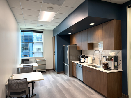 A kitchenette with a dishwasher, sink, fridge, freezer, coffee machine, two small tables with four chairs, and a window.